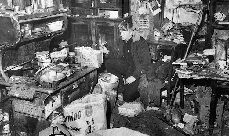 Imagen de la cocina de Gein. Se ve una estancia muy revuelta, con un policía examinándola. 