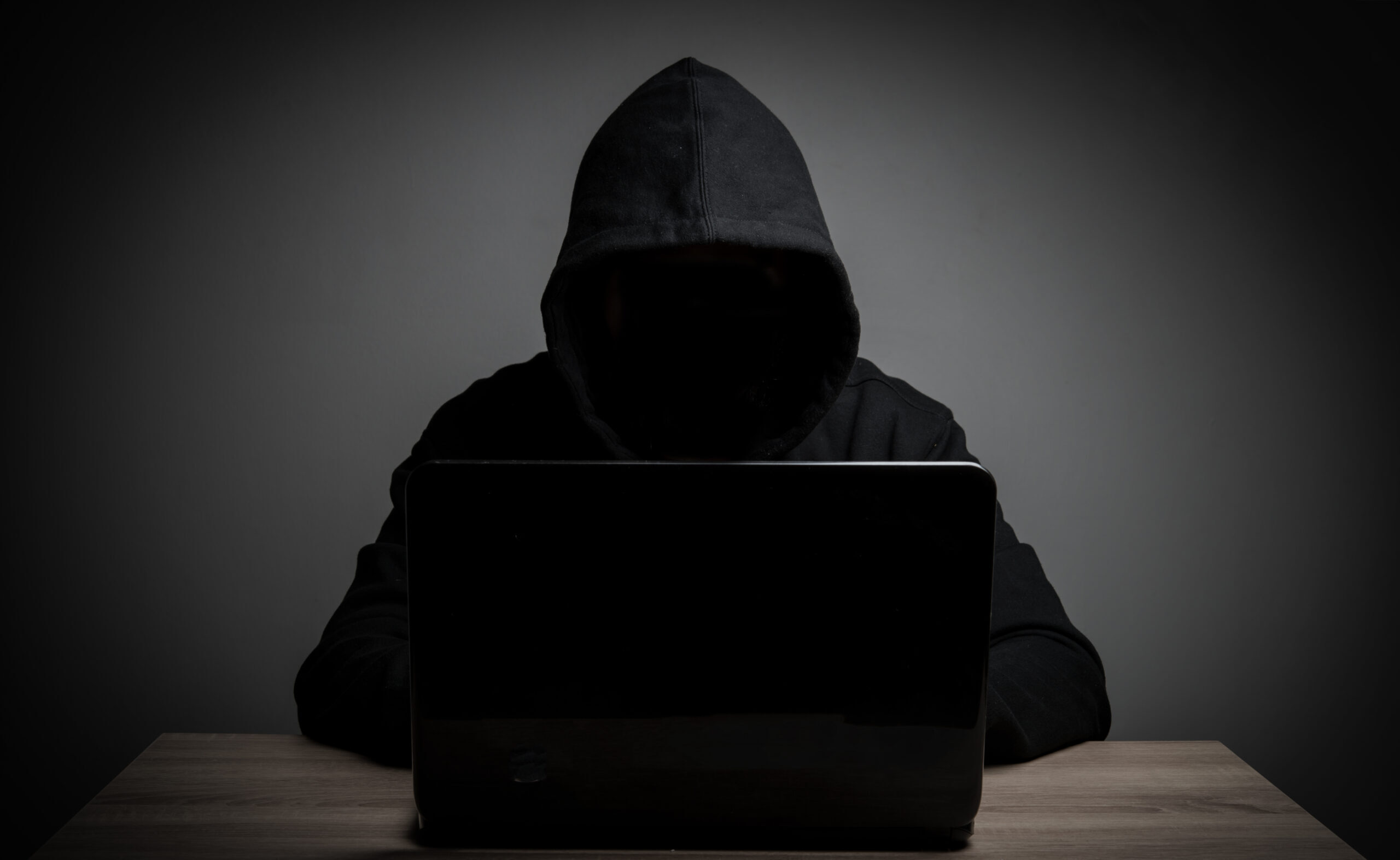 Imagen en tonos oscuros de un hombre con capucha frente a un ordenador.